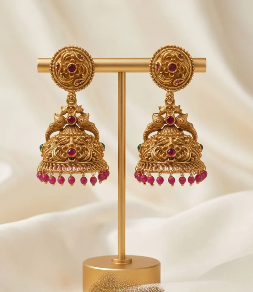 Antique Gold Plated Temple Jhumka Earrings Feature Peacock Motifs Accented With Ruby Red Bead Drops.